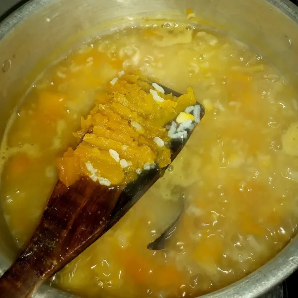 Setelah beras pecah dan labu empuk, hancurkan labu kuningnya menggunakan garpu atau tekan ke dinding panci. Bubuhi garam.