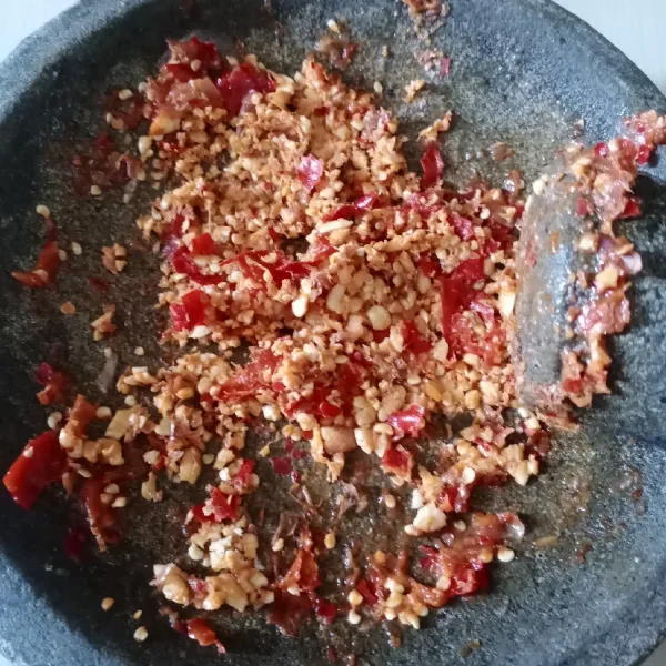Haluskan bawang merah, bawang putih, cabai rawit, dan cabai merah keriting. Kemudian masukkan kacang tanah goreng dan ulek kasar agar tekstur kacang tetap terasa.