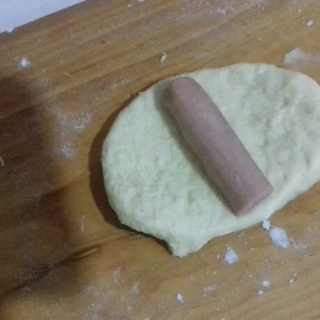 Ambil 1 bagian roti, bulatkan. Kemudian pipihkan dan letakkan sosis di tengah-tengah.