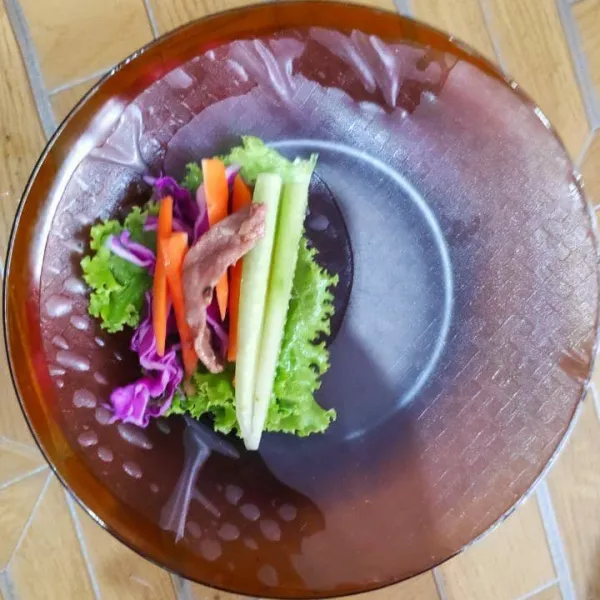 Letakan daun selada, timun, wortel, kubis ungu dan daging sapi di atas rice paper yang sudah dibasahi air.