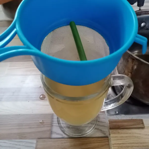 Tuang air rebusan jahe ke dalam gelas sambil disaring.