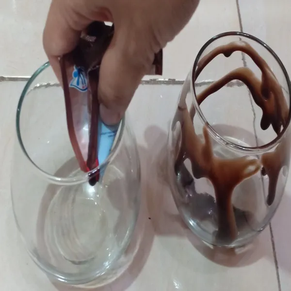 Siapkan gelas saji, lalu hiasi susu kental manis coklat dipinggiran gelasnya.
