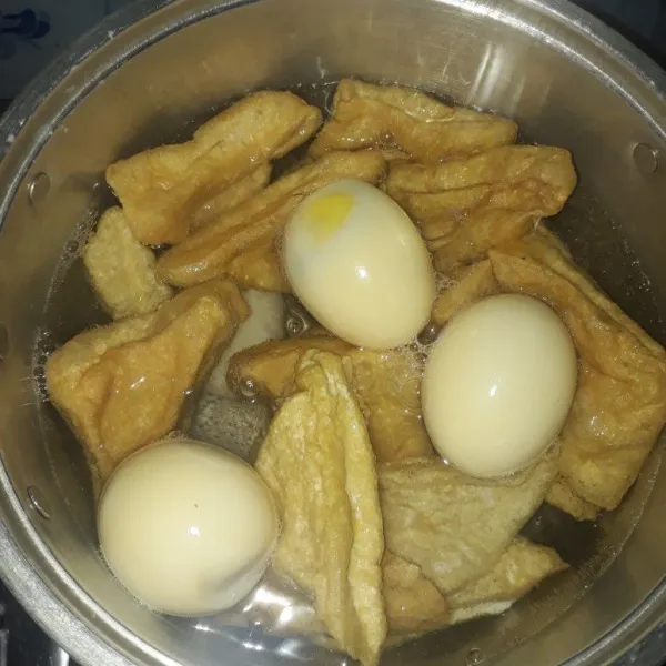 Panaskan air hingga mendidih, lalu masukkan tahu goreng dan telur rebus.