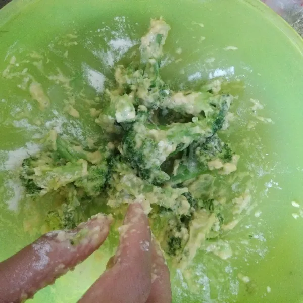Tambahkan separuh campuran tepung bumbu, aduk hingga permukaan brokoli terlumuri.