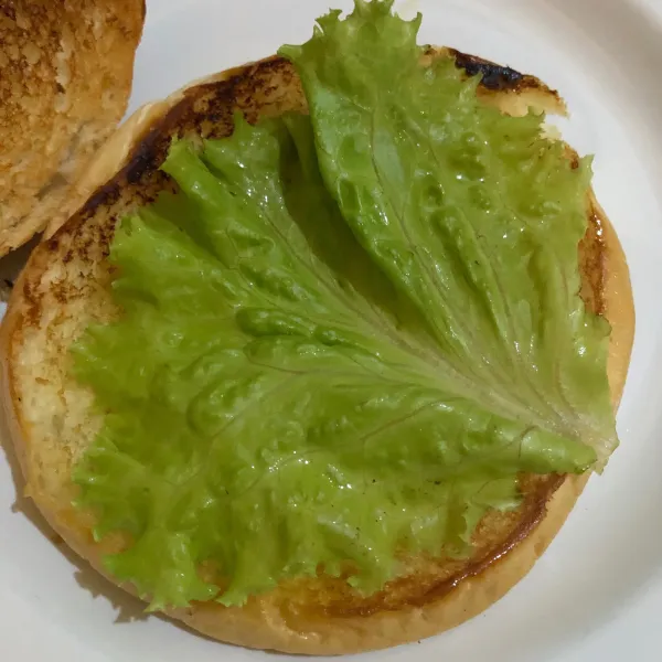 Letakkan roti burger diatas piring, lalu beri selada.