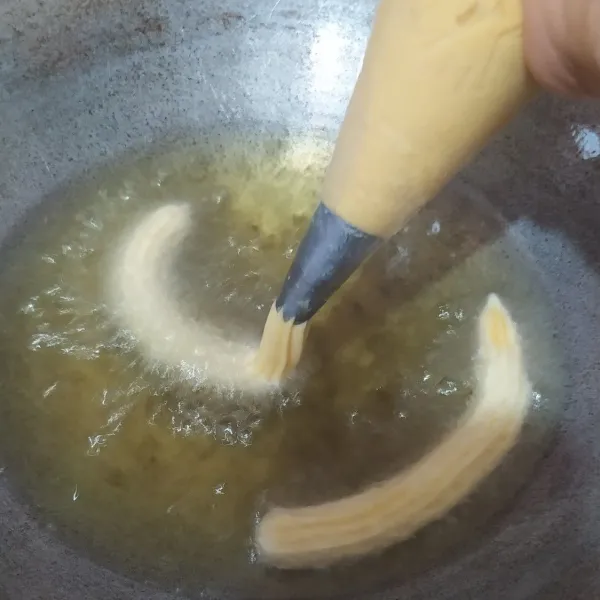 Panaskan minyak. Masukkan adonan ke kantong segitiga dan dengan bantuan spuit, semprotkan ke dalam minyak, potong dengan gunting.