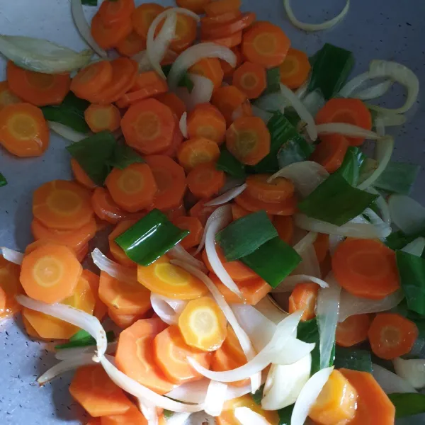 Setelah layu, masukkan daun bawang, wortel dan air. Aduk rata dan biarkan wortel setengah matang.