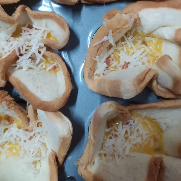 Beri potongan sosis di dalam roti tawar, tuang kocokan telur, beri taburan keju parut.