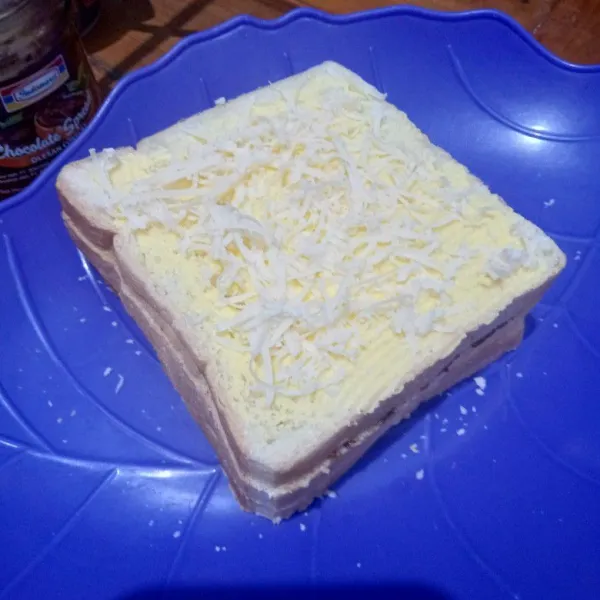 Tutup lagi dengan selembar roti tawar, olesi margarin dan beri keju parut.