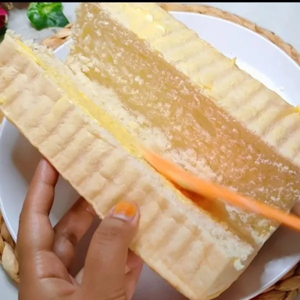 Belah tengah roti tanpa terputus, olesi merata semua sisi dan dalam dengan margarin