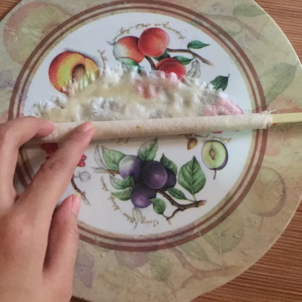 Gulung kulit lumpia menggunakan sumpit plastik, bagian atasnya olesi air