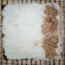 Siapkan penggulung sushi, alasi dengan plastik wrap letakkan 1 lembar rumput laut. Kemudian, pipihkan ketan di atasnya hingga rata. Tata isian lemper di atasnya.