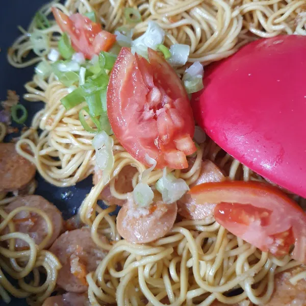Masukkan mie, aduk hingga bumbu tercampur. Tambahkan tomat dan daun bawang.