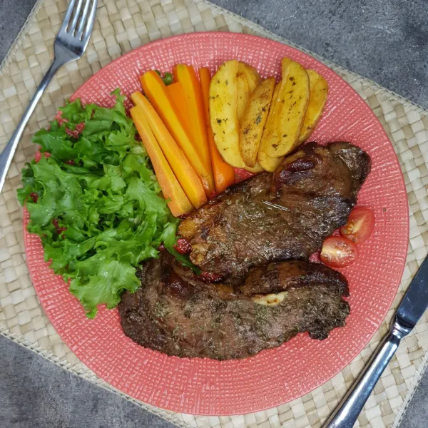 Sajikan steak bersama wortel rebus, selada, dan potato wedges.