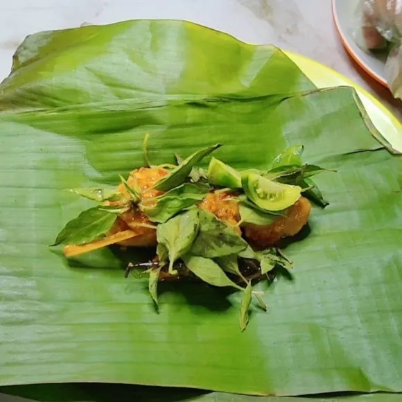 Siapkan daun pisang lalu masukkan ayam beri daun kemangi, irisan tomat dan beri bumbu dari sisa ungkepan tadi.