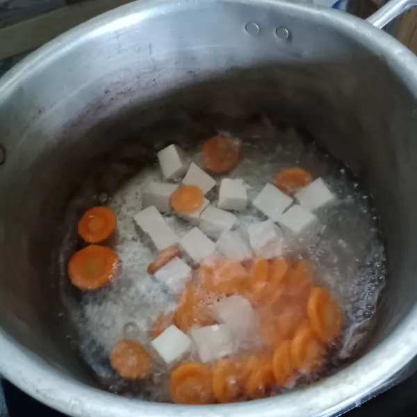 Didihkan air di panci, masukan wortel. Masak sampai wortel setengah matang kemudian masukan tahu.