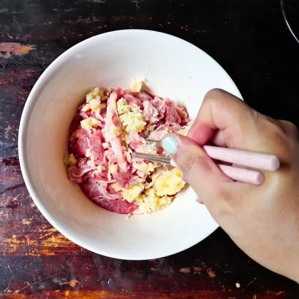 Campurkan parutan jahe dan bawang putih ke dalam wadah yang berisi daging. Aduk rata.