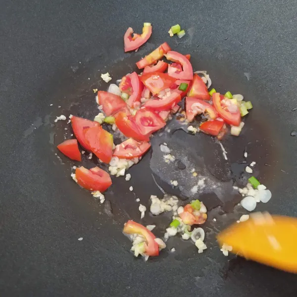 Masukan tomat yang diiris tipis dan bagian putih daun bawang. Tumis hingga layu.