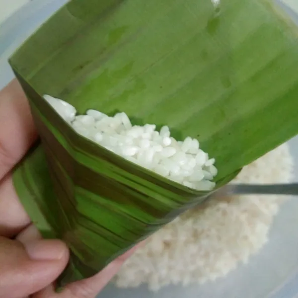 Ambil 1 lembar daun pisang lalu isi dengan beras ketan, padatkan.