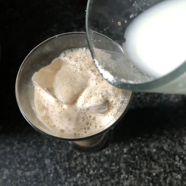 Tuang ke dalam gelas yang berisi es batu lalu beri susu cair dan juga serbuk cokelat di atasnya.