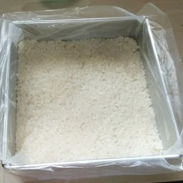 Masukan nasi ketannya setengah tinggi loyang. Tekan-tekan dengan centong nasi agar padat.