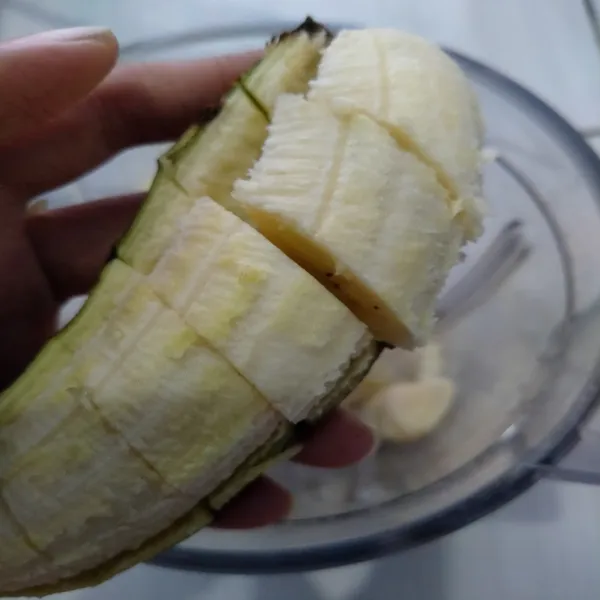 Potong-potong pisang, lalu masukkan ke dalam blender. Tambahkan es batu dan oatmilk