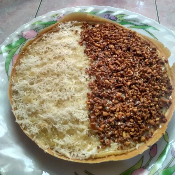 Setelah martabak matang, segera olesi dengan mentega di seluruh permukaannya. Lalu taburkan dengan keju parut, kacang dan susu kental manis.