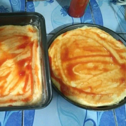 Olesi loyang dengan margarin, bentuk adonan dengan 2 loyang ratakan, tusuk tusuk adonan dengan garpu, lalu olesi peemukaannya dengan saus tomat