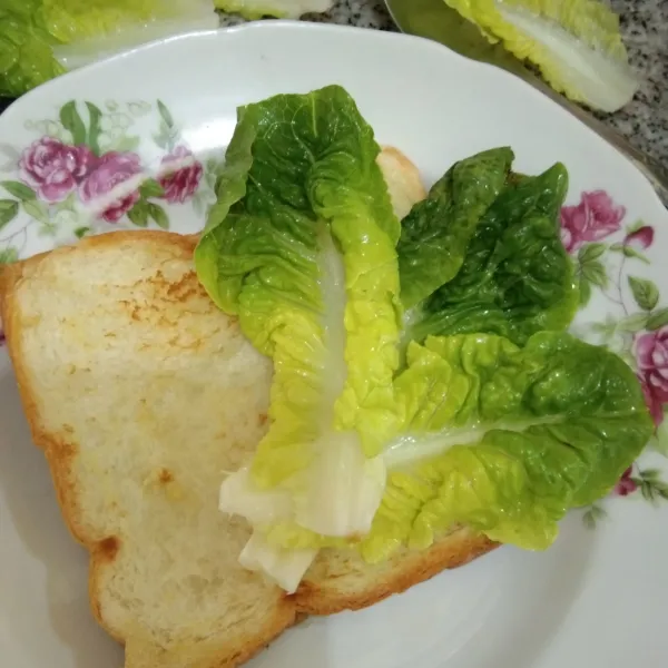 Siapkan roti yang telah dipanggang, tata daun selada di pinggir roti