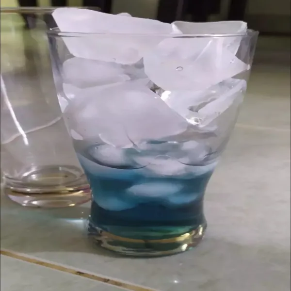 Tuang larutan bunga telang hingga 1/4 bagian gelas, kemudian masukkan es batu hingga melebihi bibir gelas