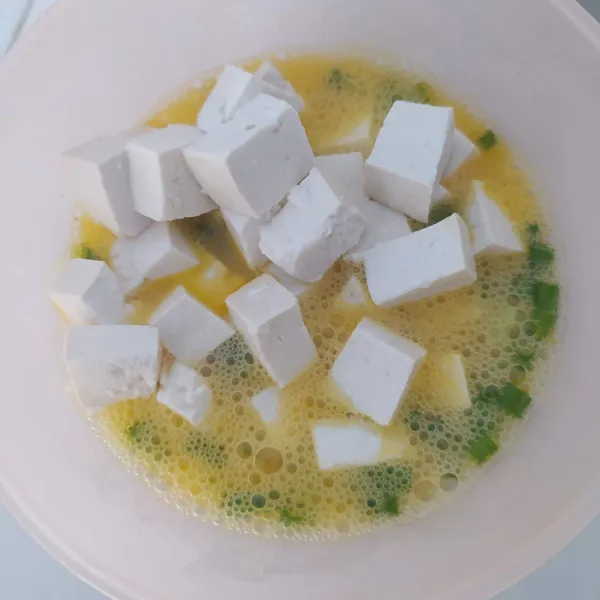 Pecahkan telur dalam mangkok, tambahkan irisan daun bawang, garam dan merica, kocok lepas. Masukkan tahu, aduk rata.