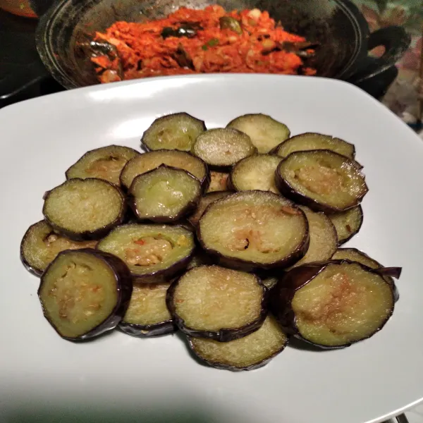 Tata terong yang sudah digoreng dalam wadah saji, siram dengan tongkol suwir. Sajikan.