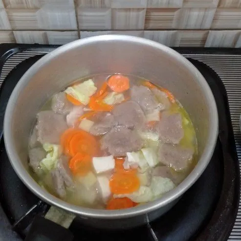 Masukan air, wortel dan kentang secara bersamaan. Masak hingga lembut lalu masukan potongan Bakso serta ayam.