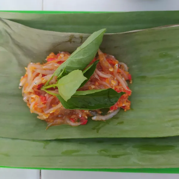 Siapkan daun pisang yang sudah dibersihkan, letakkan teri nasi berbumbu diatasnya, tambahkan kemangi, bungkus sesuai selera.