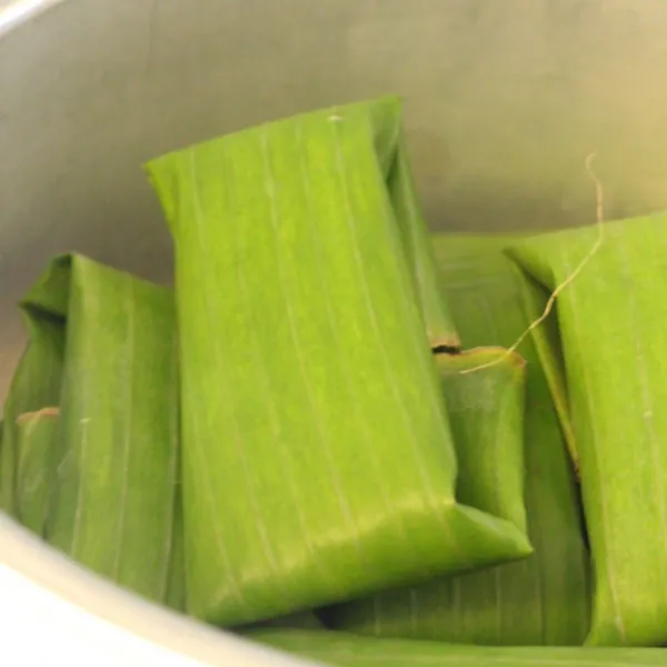 Bungkus mengelilingi adonan hingga semua terbungkus lalu lipat atas bawah ke bagian bawah, tata di kukusan.