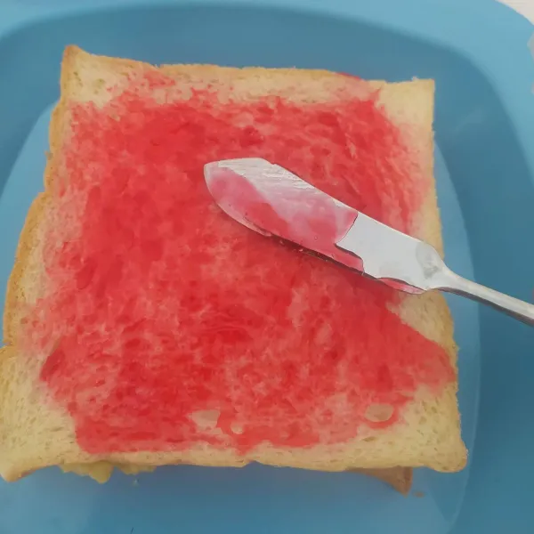 Tutup atasnya dengan selembar roti tawar, olesi dengan selai strawberry.