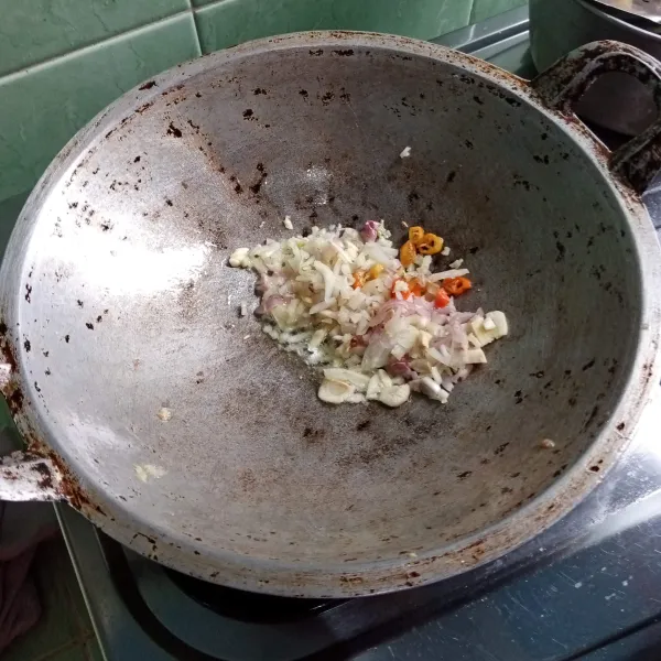 Panaskan minyak goreng. Masukkan bawang putih, bawang merah, cabe rawit, dan bawang bombai yang sudah dipotong-potong tadi. Tumis hingga layu.