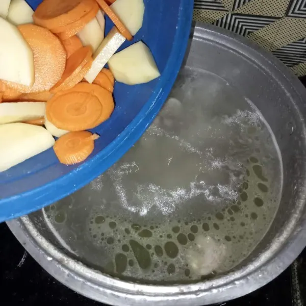 Kupas dan potong-potong kentang dan wortel, lalu masukkan ke dalam panci.