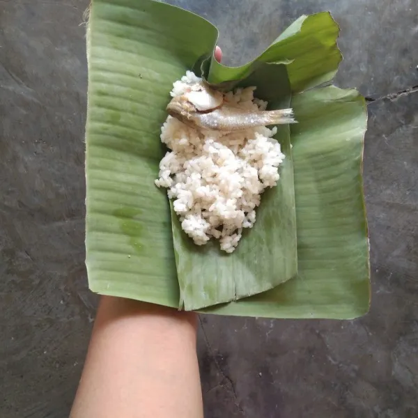 Letakkan nasi pada daun pisang dan tambahkan ikan asin.