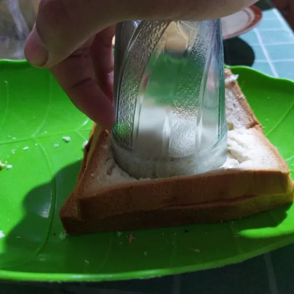 Ambil gelas belimbing kemudian tekan tepat ditengah roti tawar hingga kedua roti merekat.