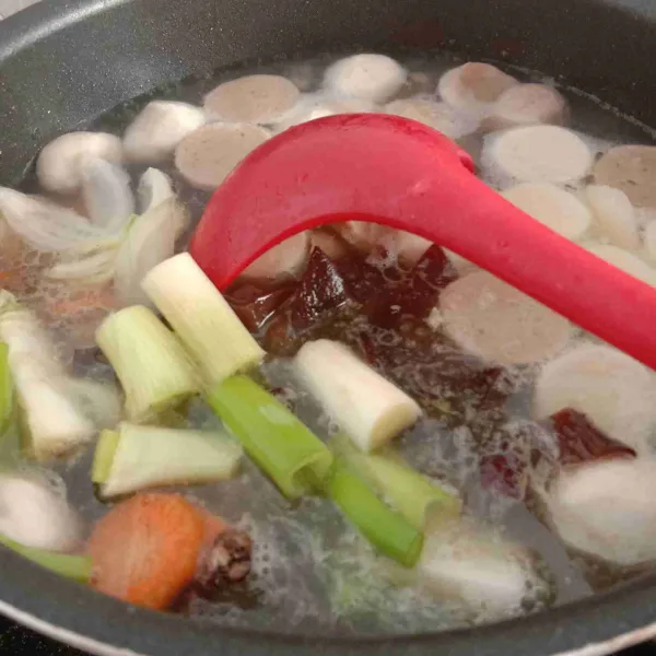 Tambahkan air, masukkan bakso ikan, bakso sapi, wortel, kentang, daun bawang, bawang pre, bawang bombay, dan jamur. Biarkan hingga mendidih.