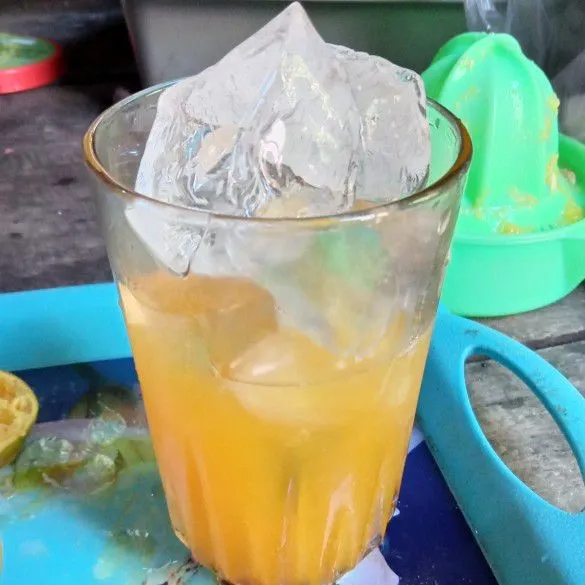 Masukkan es batu ke dalam gelas hingga penuh, lalu tuang air jeruk hingga setengah gelas.
