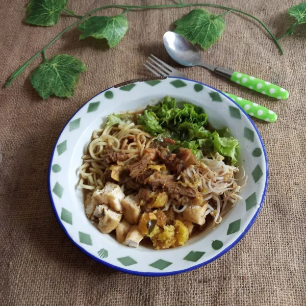 Ambil 1-2 sdm bumbu petis ratakan dipiring, beri mie kuning, irisan selada, taoge seduh, tahu goreng dan perkedel singkong yang sudah dipotong-potong. siram dengan kuah berisi tetelan sapi. Sajikan hangat