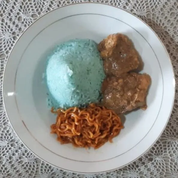 Siapkan piring saji. Tata nasi uduk biru bunga telang di dalam piring, lengkapi dengan lauk pauk lainnya. Siap dihidangkan.