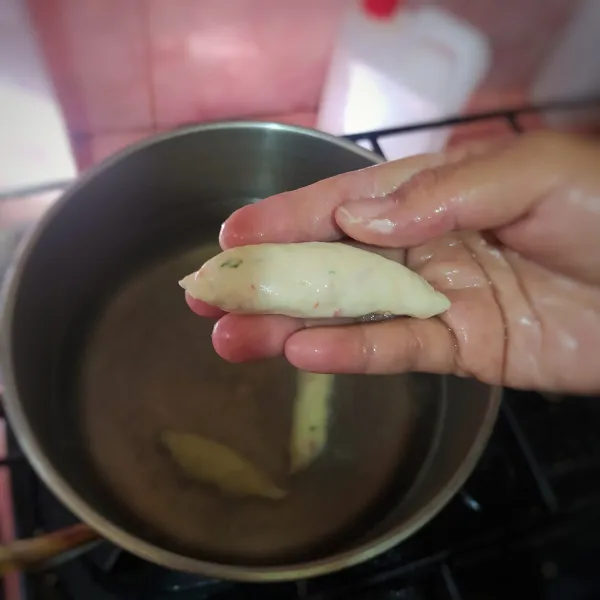 Olesi tangan dengan minyak, lalu bentuk memanjang. Masukkan ke panci berisi air panas.