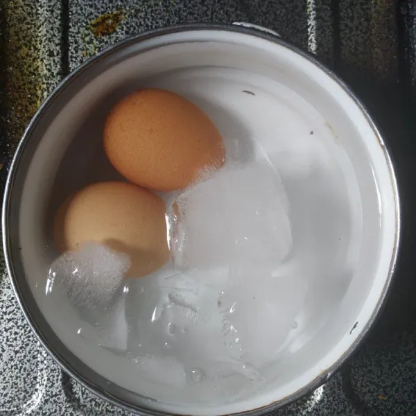 Siapkan wadah yang berisi air dan es batu, rendam telur rebus.