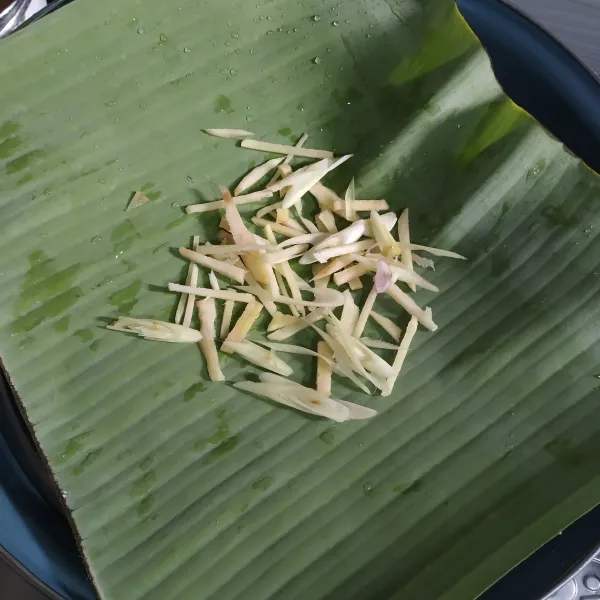 Letakan piring tahan panas, alasi dengan daun pisang. Lalu letakan potongan jahe, serai dan juga lengkuas