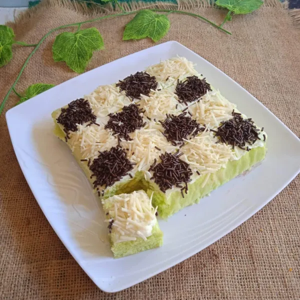Keluarkan dari loyang saat sudah hangat. Oles dengan buttercream lalu garis-garis dan hiasi dengan keju parut dan meises coklat berselang-seling.