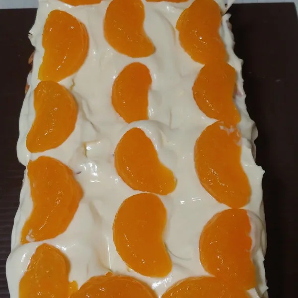 Tuang whipping cream di atas cake ratakan, lalu beri toping jeruk atau buah segar lainnya