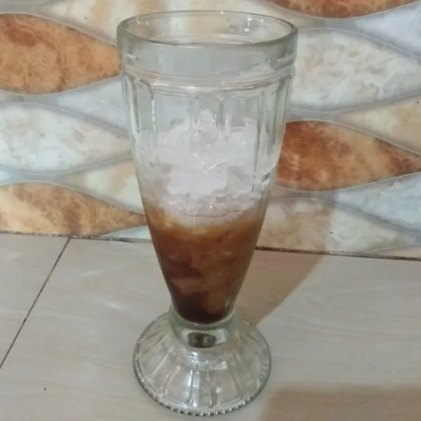 Tuang sirup gula merah ke dalam gelas saji, lalu tambahkan potongan es batu.